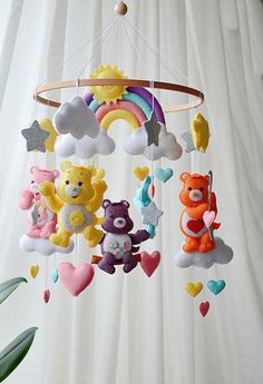 a crib mobile with teddy bears and rainbows hanging from the ceiling next to a potted plant