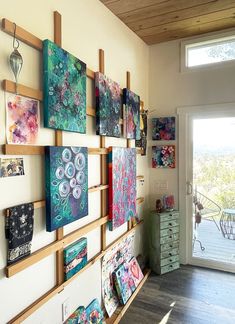 the wall is filled with colorful paintings on it's sides and hanging from wooden shelves