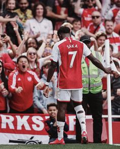 a soccer player is standing on the field with his hands in the air and fans behind him