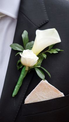 a boutonniere with a white rose and green leaves on the lapel