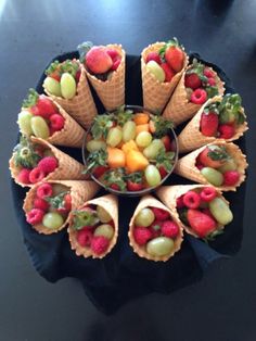 an arrangement of fruit in cones on top of a black table with a bowl of strawberries and grapes