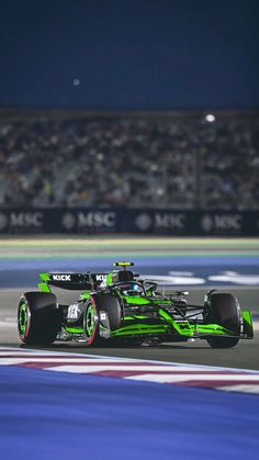 a green race car driving on a track at night time with spectators in the background