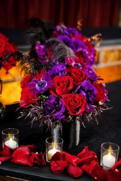 red and purple flowers are in vases on a table with two votive candles