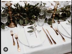 the table is set with silverware and greenery