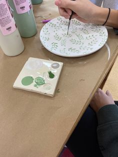 a person painting on a white plate with green leaves