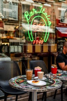 two people sitting at a table in front of a restaurant with neon signs behind them