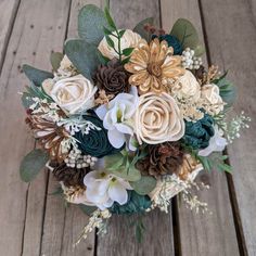 a bridal bouquet with flowers and greenery on a wooden surface, ready to be used as a wedding bouquet