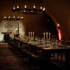 a long table is set with wine glasses and candles in front of an arched wall