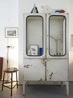 an old white cabinet with glass doors in a room next to a chair and table