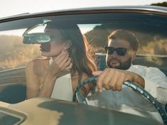 a man and woman sitting in the driver's seat of a car, both wearing sunglasses