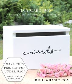 a white card box sitting on top of a table with pink flowers in front of it