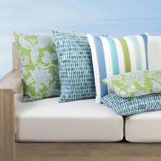 a white couch with green and blue pillows on it's back end, next to a wooden railing