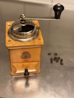 an old coffee grinder sitting on top of a metal table next to some coffee beans