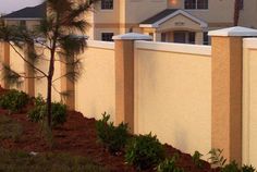 a white fence with trees and bushes in front of a house at dusk, next to a palm tree