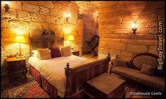 a bedroom with stone walls and flooring is lit by two lamps on either side of the bed