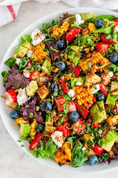 a salad with corn, blueberries, and avocado in a white bowl