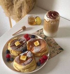 pancakes with butter and berries on a plate next to a cup of coffee