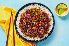 a blue bowl filled with rice and meat next to chopsticks on a yellow napkin