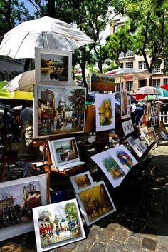 there are many paintings on display under an umbrella