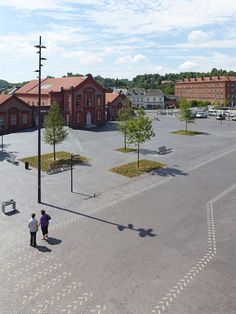 two people are standing in the middle of a parking lot near some trees and buildings