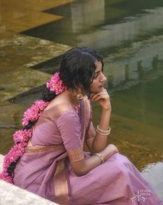 a woman sitting on the edge of a body of water with flowers in her hair