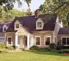 a white house with black shingles on the roof and two story windows, surrounded by green grass