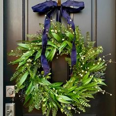 a wreath with blue ribbon hanging on the front door to a house that is decorated with greenery