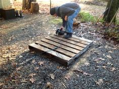 a man is working on a wooden pallet in the woods near a tent and trees