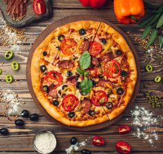 a pizza sitting on top of a wooden cutting board next to tomatoes and olives