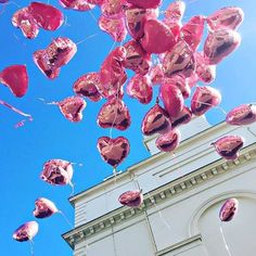 many pink heart shaped balloons are floating in the air near a white building and blue sky