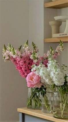 some pink and white flowers are in vases on a table with shelves behind them