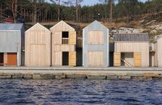 several wooden buildings sitting on the side of a body of water next to a forest