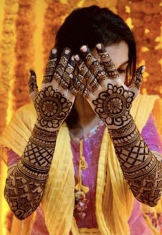 a woman with henna on her hands and hand covering her face, in front of a yellow wall