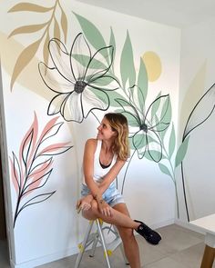 a woman sitting on a chair in front of a wall with flowers painted on it