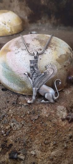 a silver necklace with a bird on it sitting on top of a rock next to two rocks