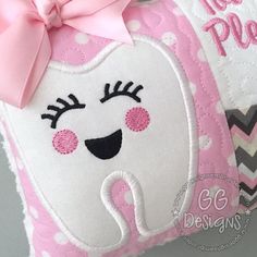 a tooth pillow with a pink bow on the front and white teeth on the back