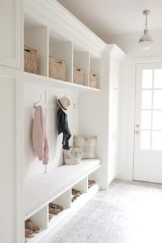 a white entryway with shoes, coat rack and baskets hanging on the wall next to it