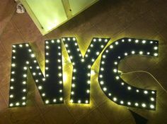 the letters nyc are lit up with lights and plugged in to the floor below them