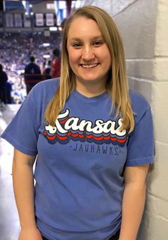 a woman standing in front of a wall wearing a kansas t - shirt