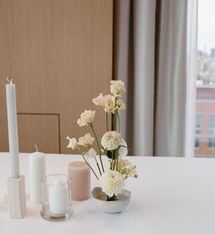 white flowers and candles on a table in front of a window with cityscape