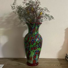 a green vase with flowers in it sitting on a table next to a stack of books