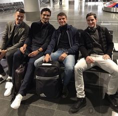 four men sitting on a bench in an airport waiting for their luggage to be picked up