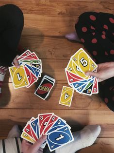 two people holding playing cards on top of a wooden floor with their feet in the air