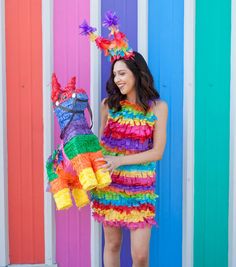 a woman in a colorful dress standing next to a rainbow colored wall with a horse decoration on it