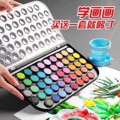 a person is holding a watercolor paint set