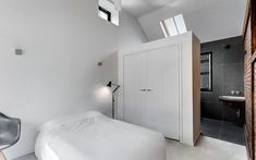 a white bed sitting under a skylight in a bedroom next to a sink and window