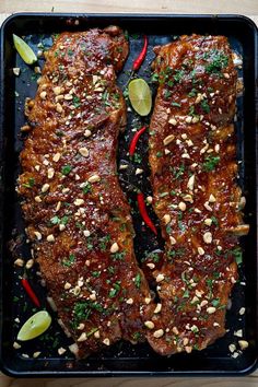 two pieces of meat on a tray with garnishes and sliced limes