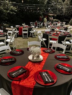 a table set up with red plates and black napkins for an outdoor dinner party