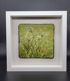 a white frame holding a painting with flowers and grass in the background on a black surface