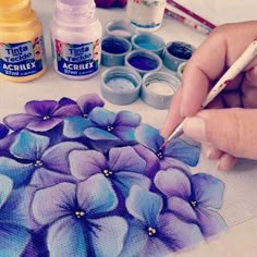 a person is painting flowers with acrylic paint and watercolors on the table